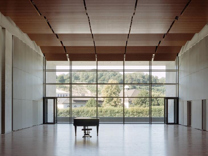 Leerer Solitär, Parkettboden, große Fensterfront, davor ein Piano | © Andrew Phelps