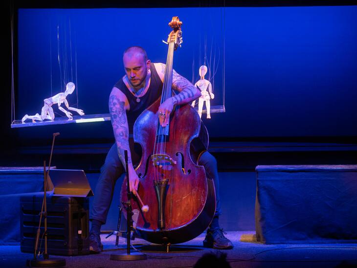 Musiker mit Kontrabass, neben ihm zwei Holzmarionetten | © Christian Schneider