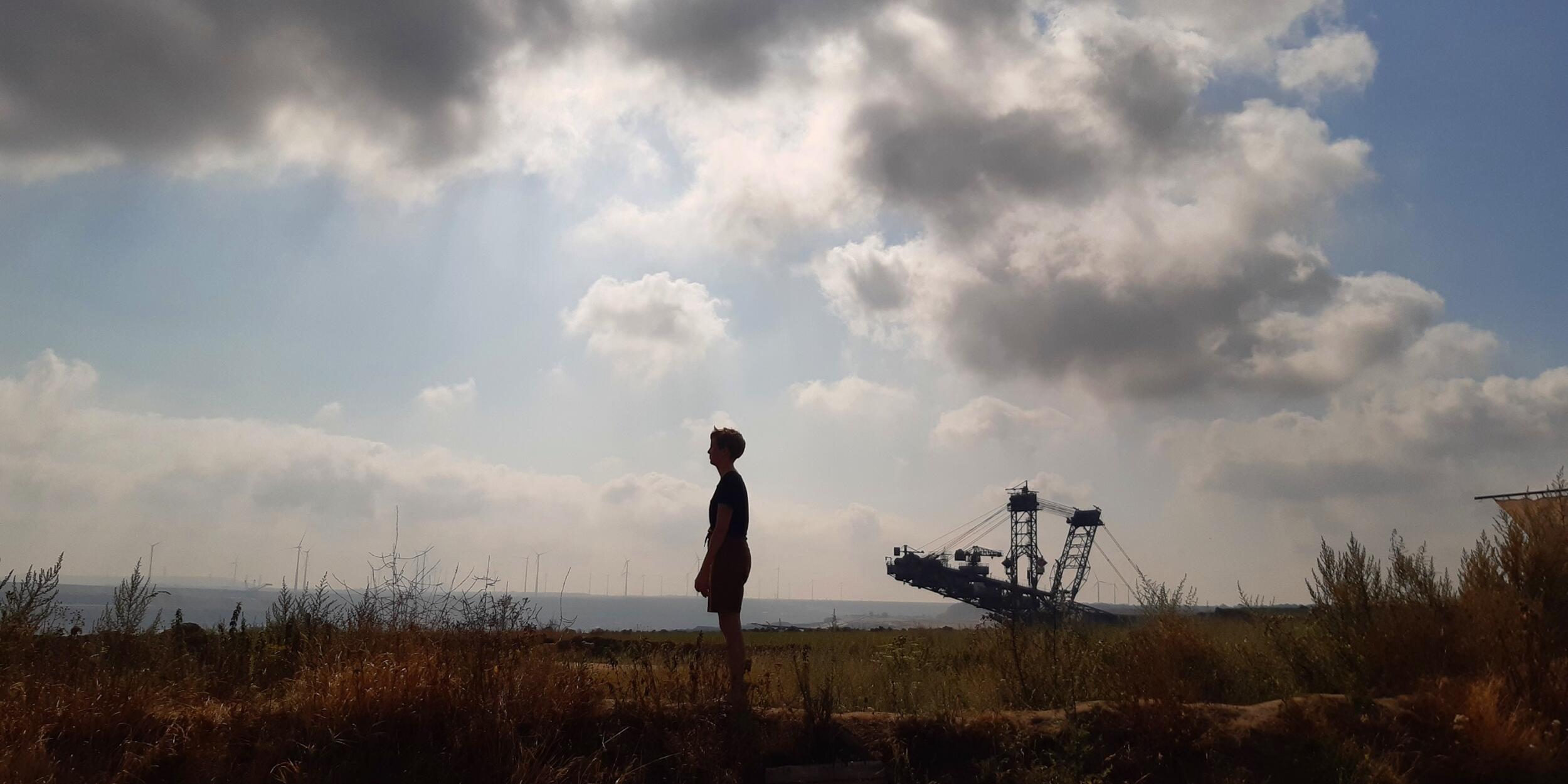 Weite, flache Landschaft, Wolken am Himmel, Silhouette eines Menschen in der Mitte