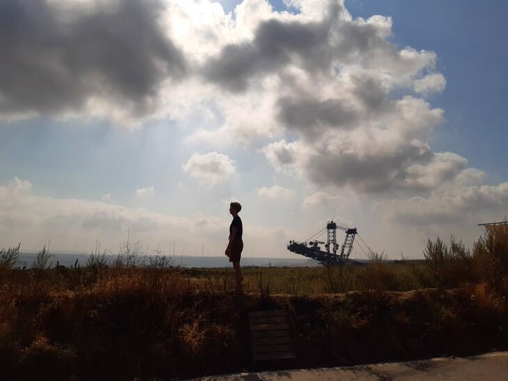 Weite, flache Landschaft, Wolken am Himmel, Silhouette eines Menschen in der Mitte