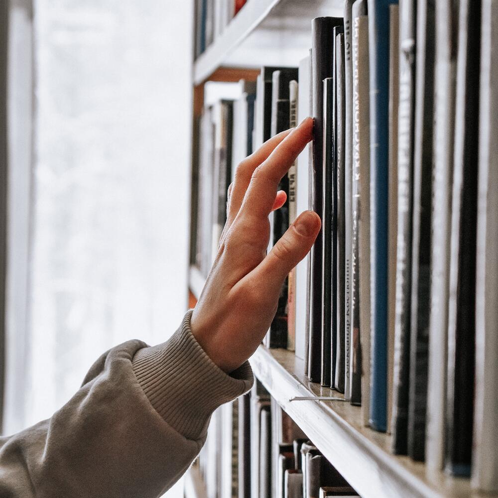 Hand greift nach einem Buch im Regal | © Guzel Maksutova