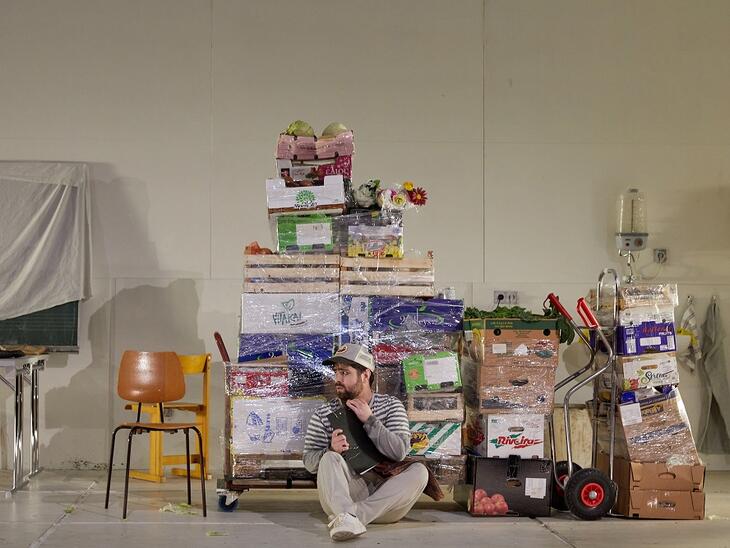 Oper: Albert Herring | © Judith Buss Mann sitzt vor eingepackten Paletten mit Lebensmitteln | © Judith Buss
